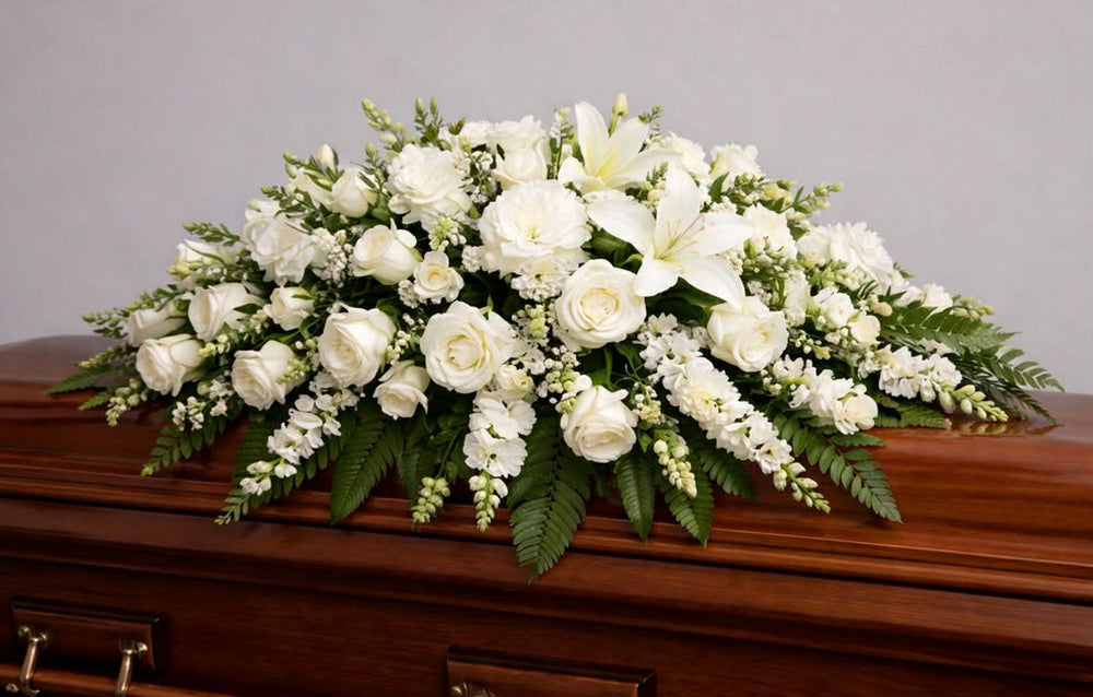 White floral arrangement on a wooden casket against a gray background